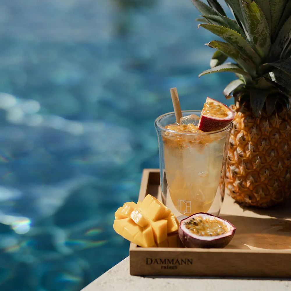 Verre d'infusion glacée au bord d'une piscine avec un ananas en fond